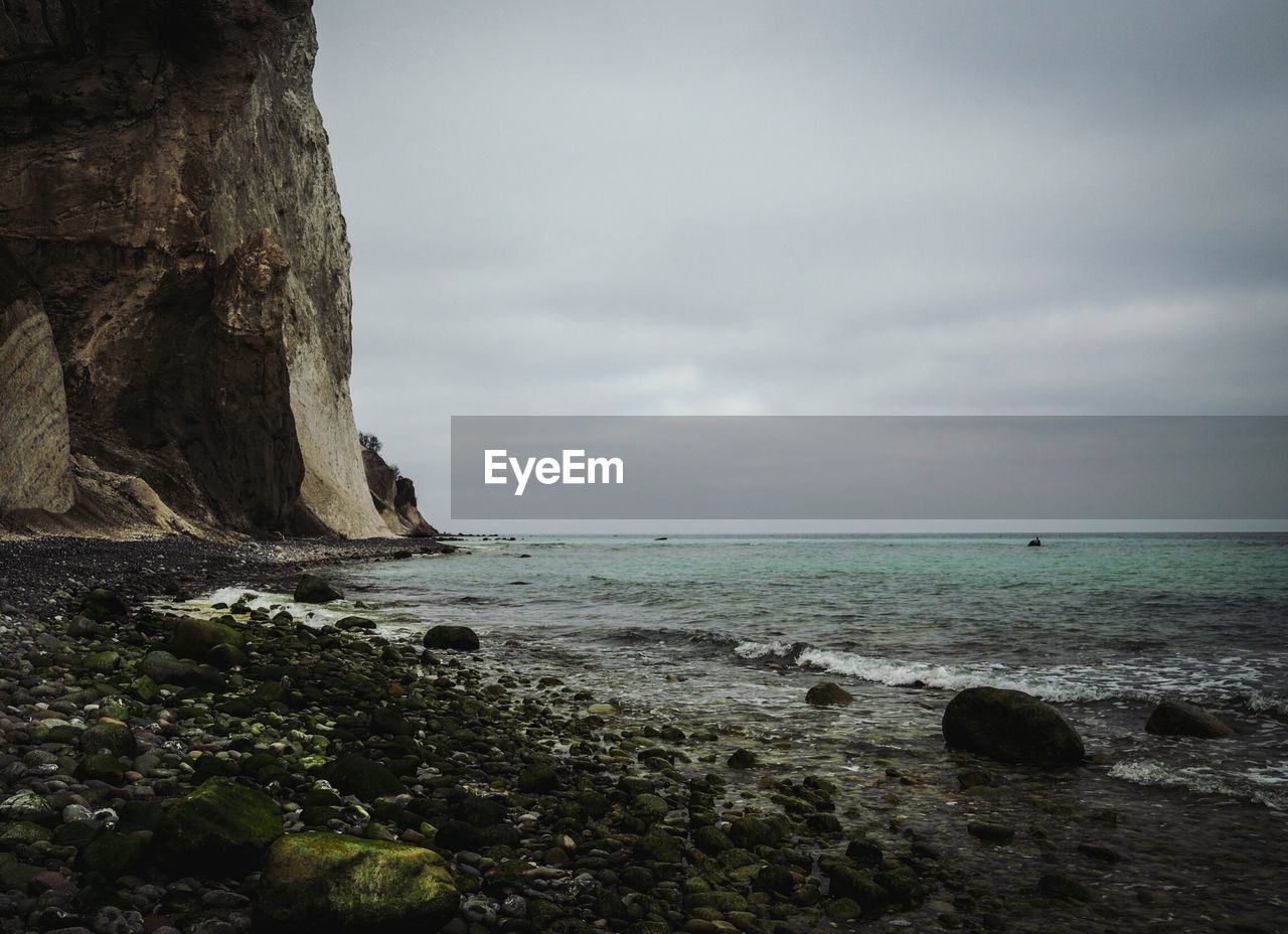 Scenic view of cliff by sea against cloudy sky