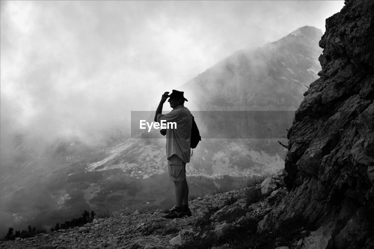 Full length of man standing on mountain against cloudy sky