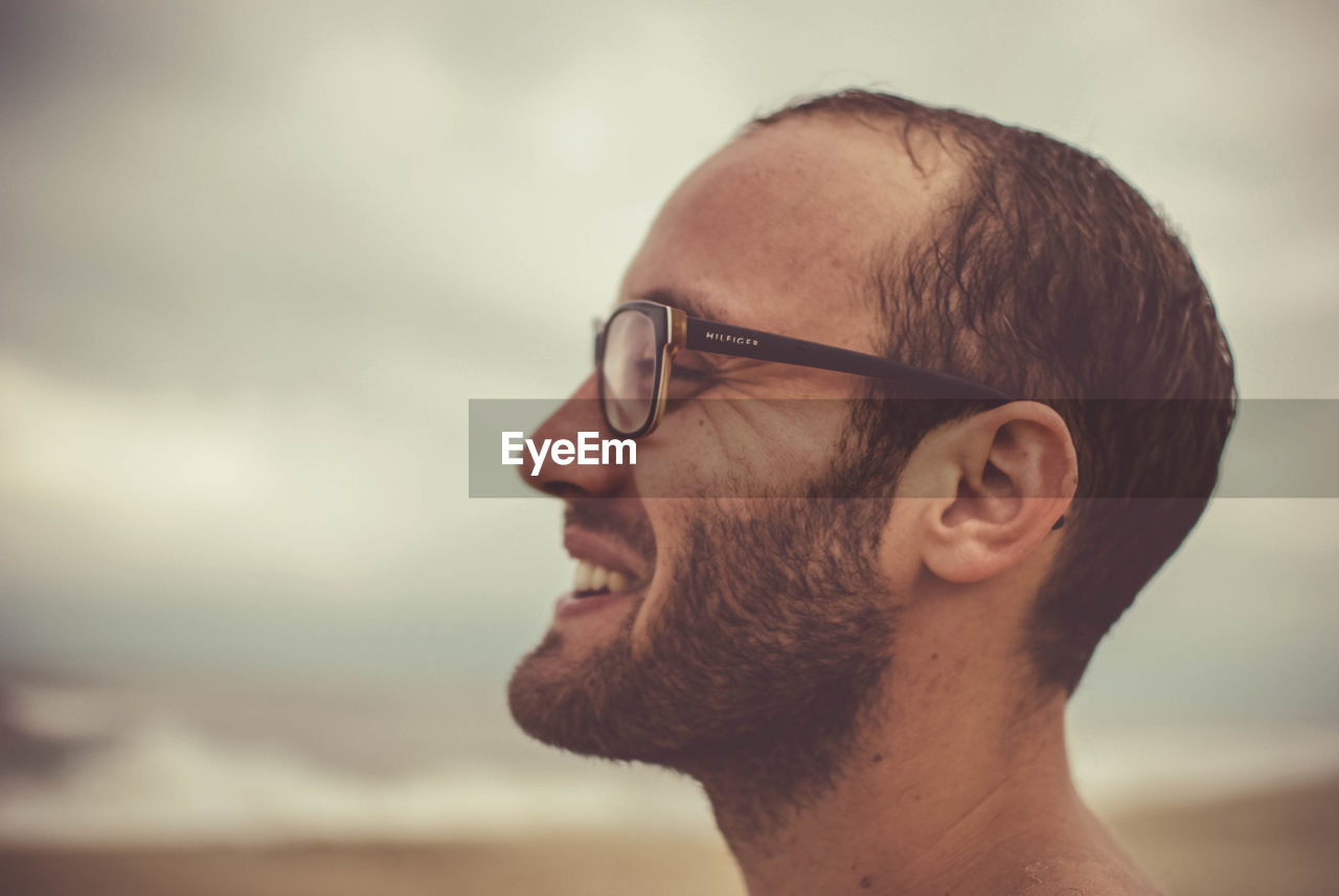 SIDE VIEW OF YOUNG MAN WEARING EYEGLASSES AGAINST SKY