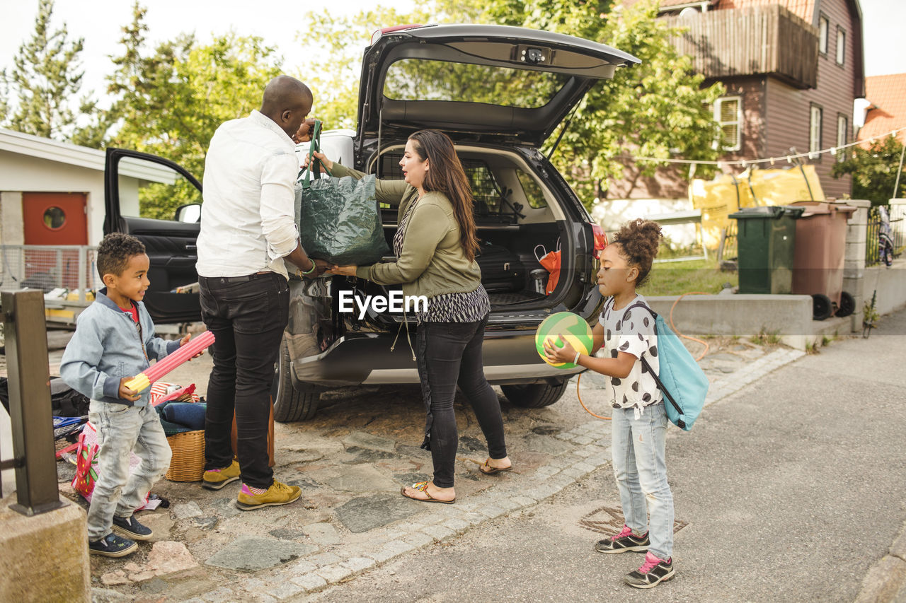 Siblings playing while parents loading luggage in car trunk on driveway