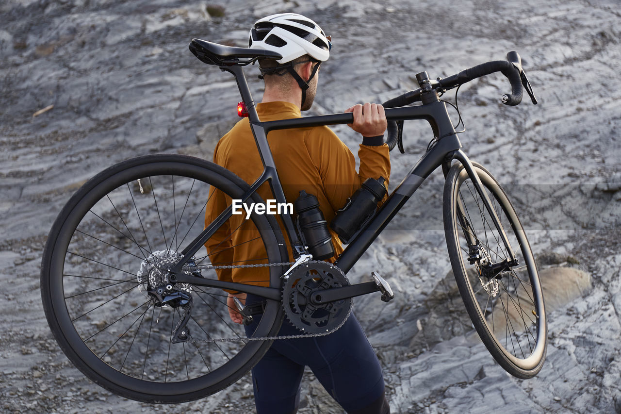 Young cyclist carrying bicycle standing on rock