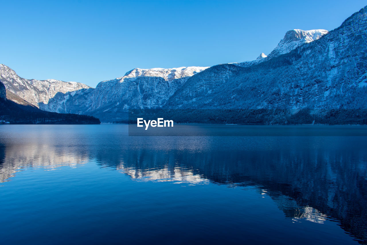 REFLECTION OF MOUNTAINS IN LAKE AGAINST BLUE SKY