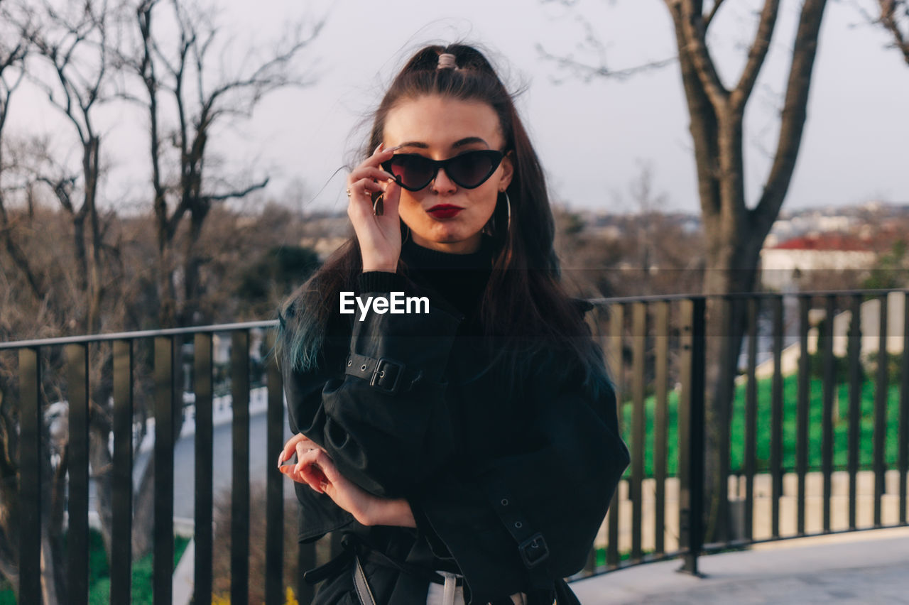 PORTRAIT OF BEAUTIFUL YOUNG WOMAN STANDING BY RAILING