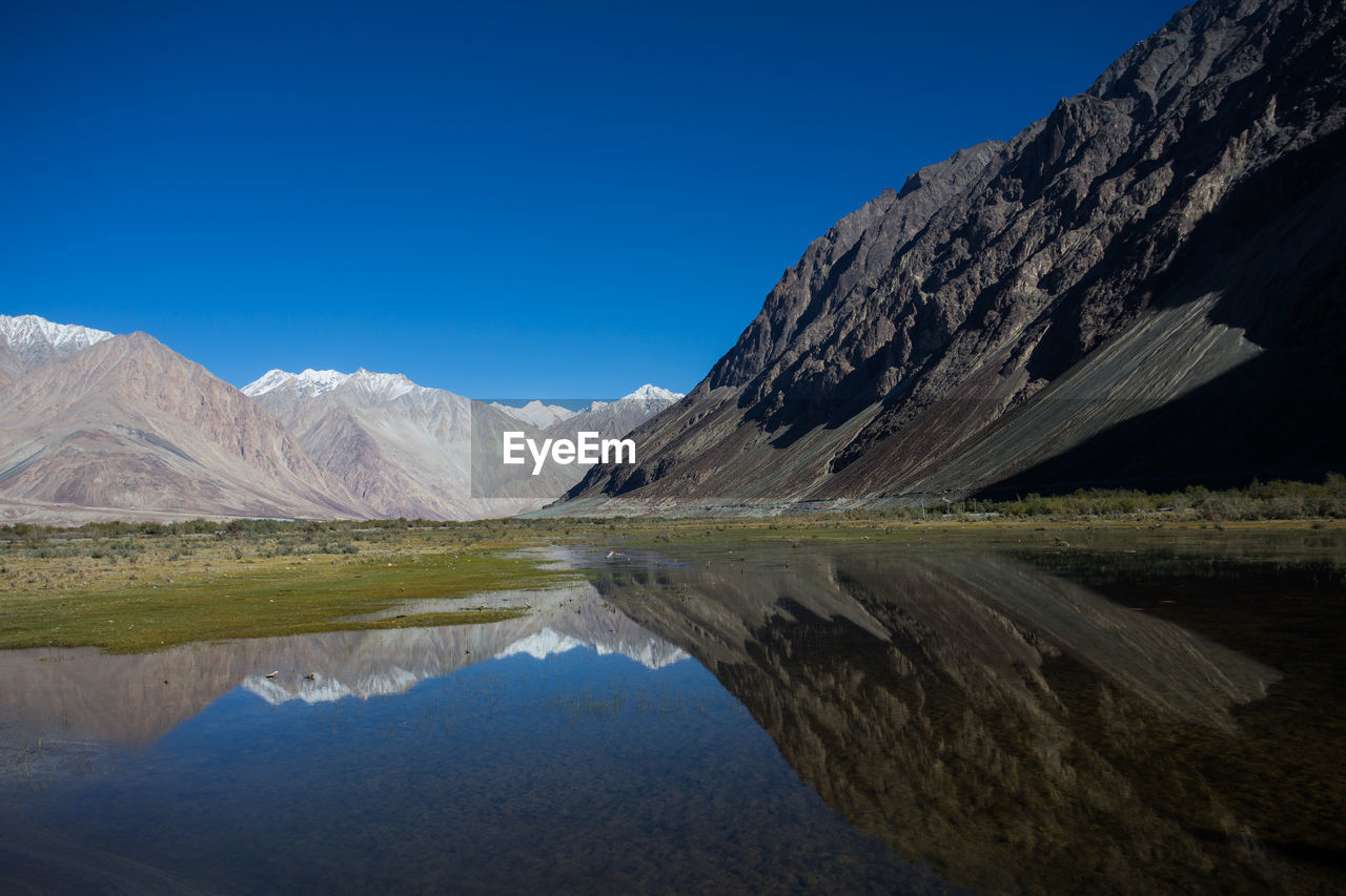 Scenic view of lake and mountains against clear blue sky