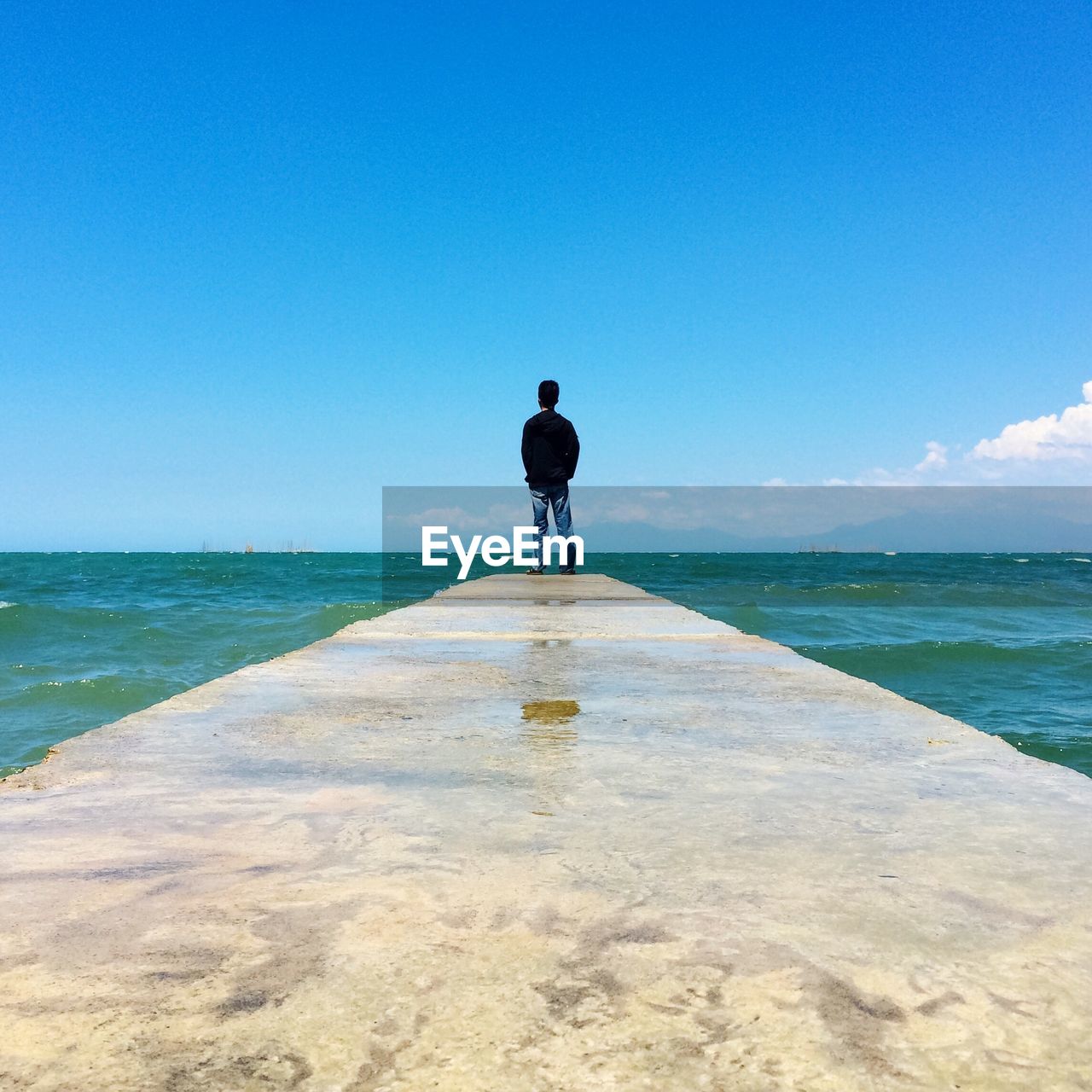 REAR VIEW OF MAN STANDING ON BEACH AGAINST CLEAR SKY