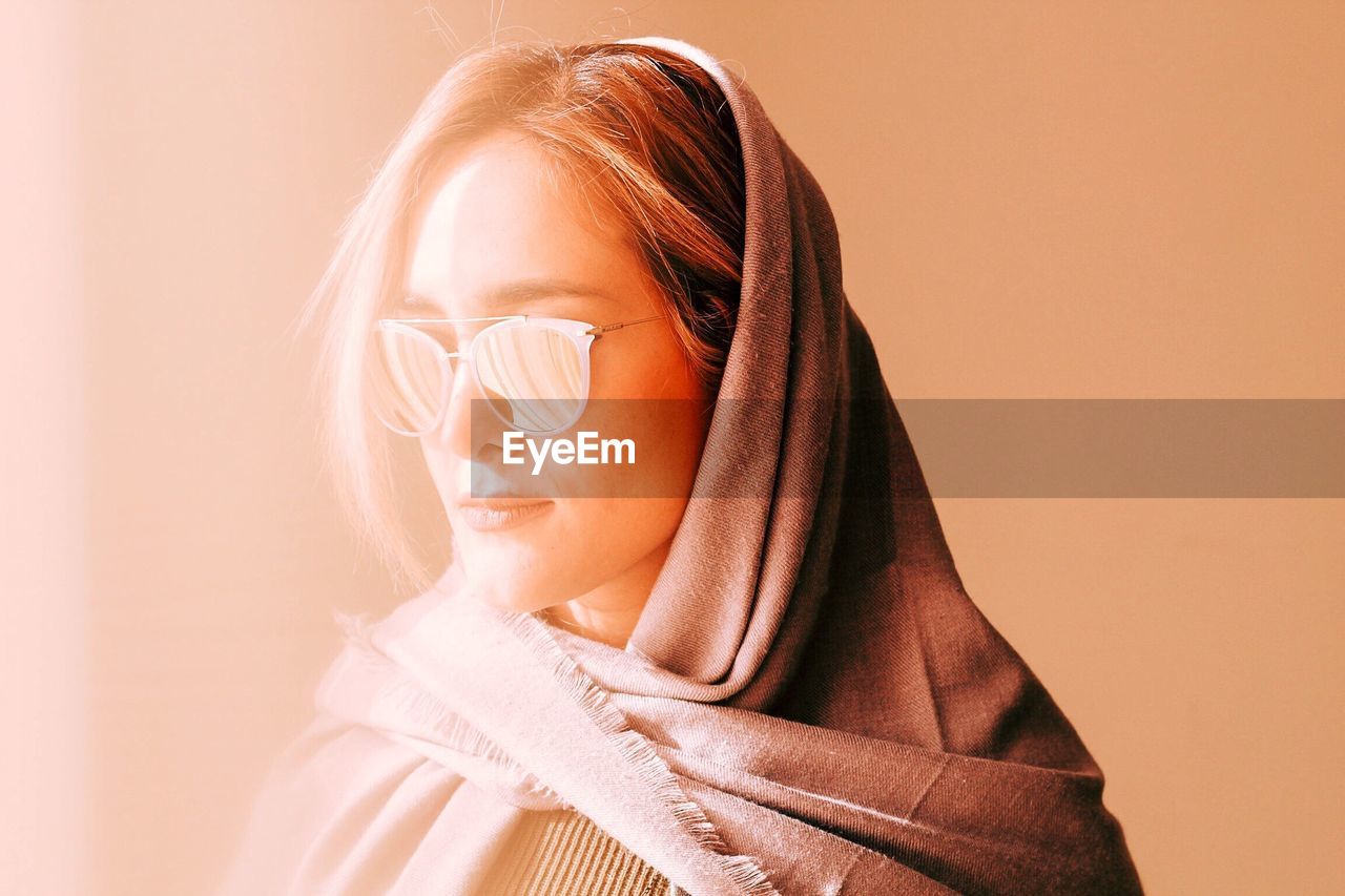 Close-up of beautiful woman in sunglasses and scarf against wall