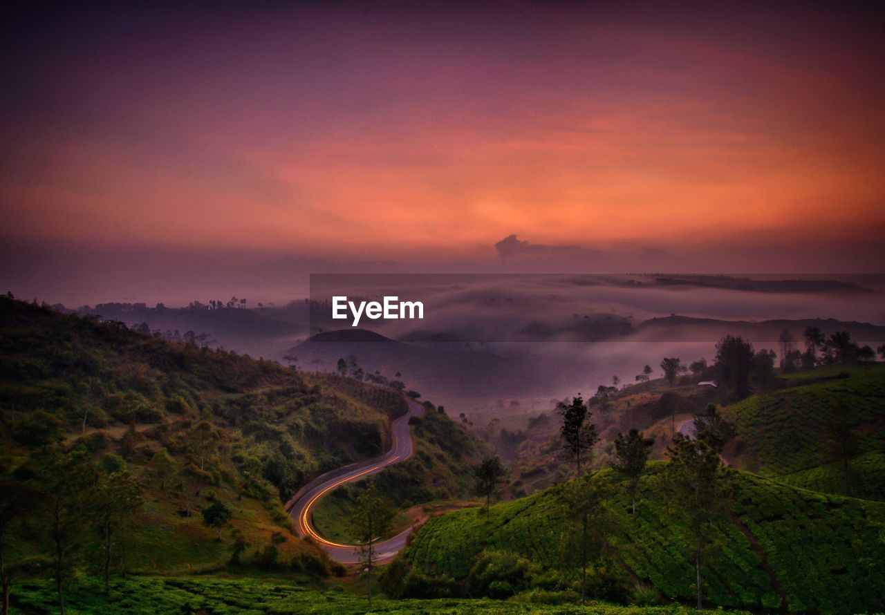 Scenic view of landscape against cloudy sky during sunset