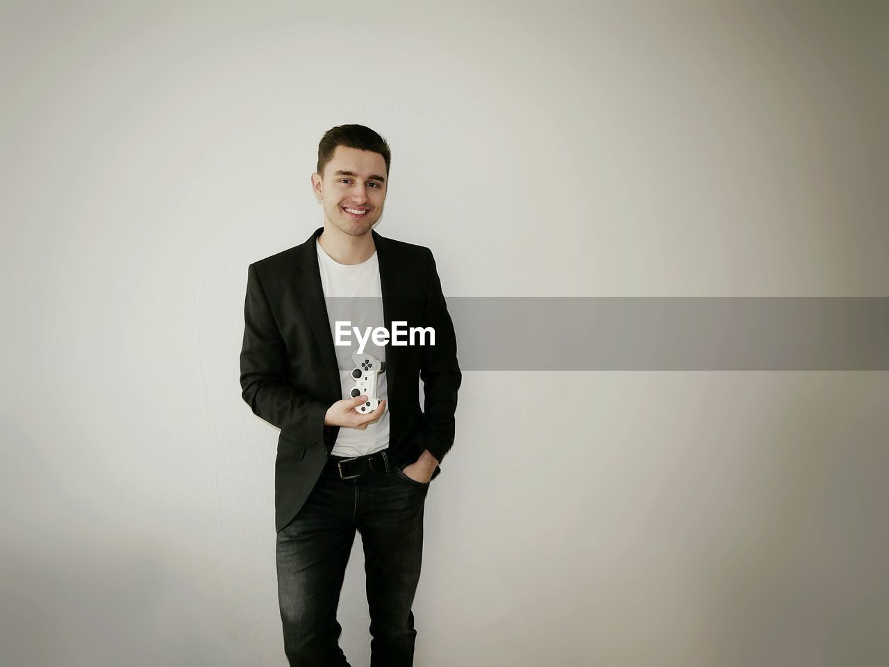 Portrait of smiling man holding remote while standing against gray background