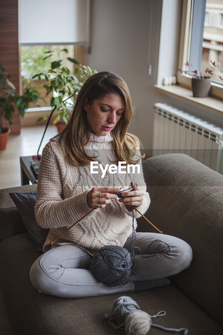 Mid adult woman knitting while sitting on sofa at home