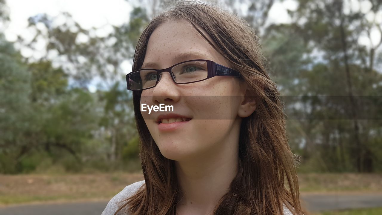 Close-up of girl looking away while standing against trees