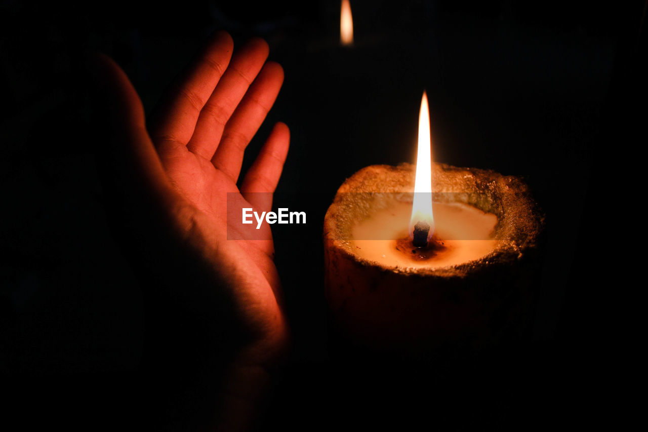 Close-up of hand shielding lit diya in darkroom