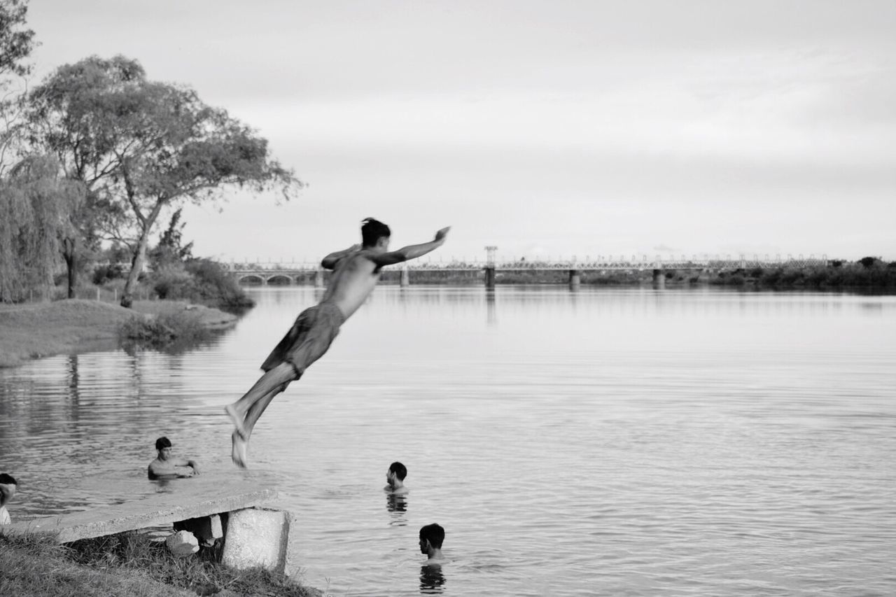 REAR VIEW OF MAN JUMPING ON LAKE