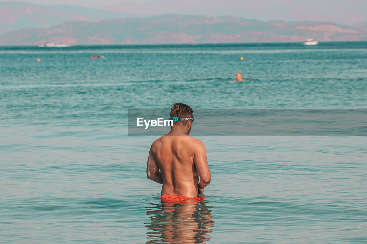 Rear view of shirtless man swimming in sea