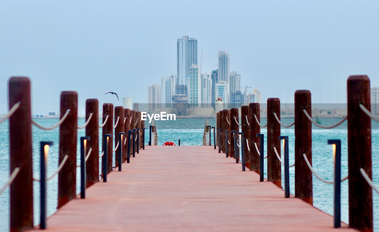 Wooden pier in sea against clear sky. waterfront view of manama, bahrain