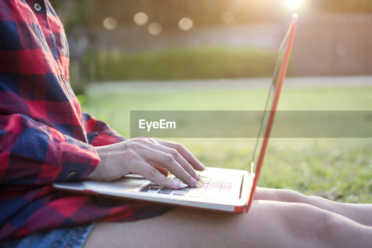 Midsection of woman using laptop while sitting on field at park