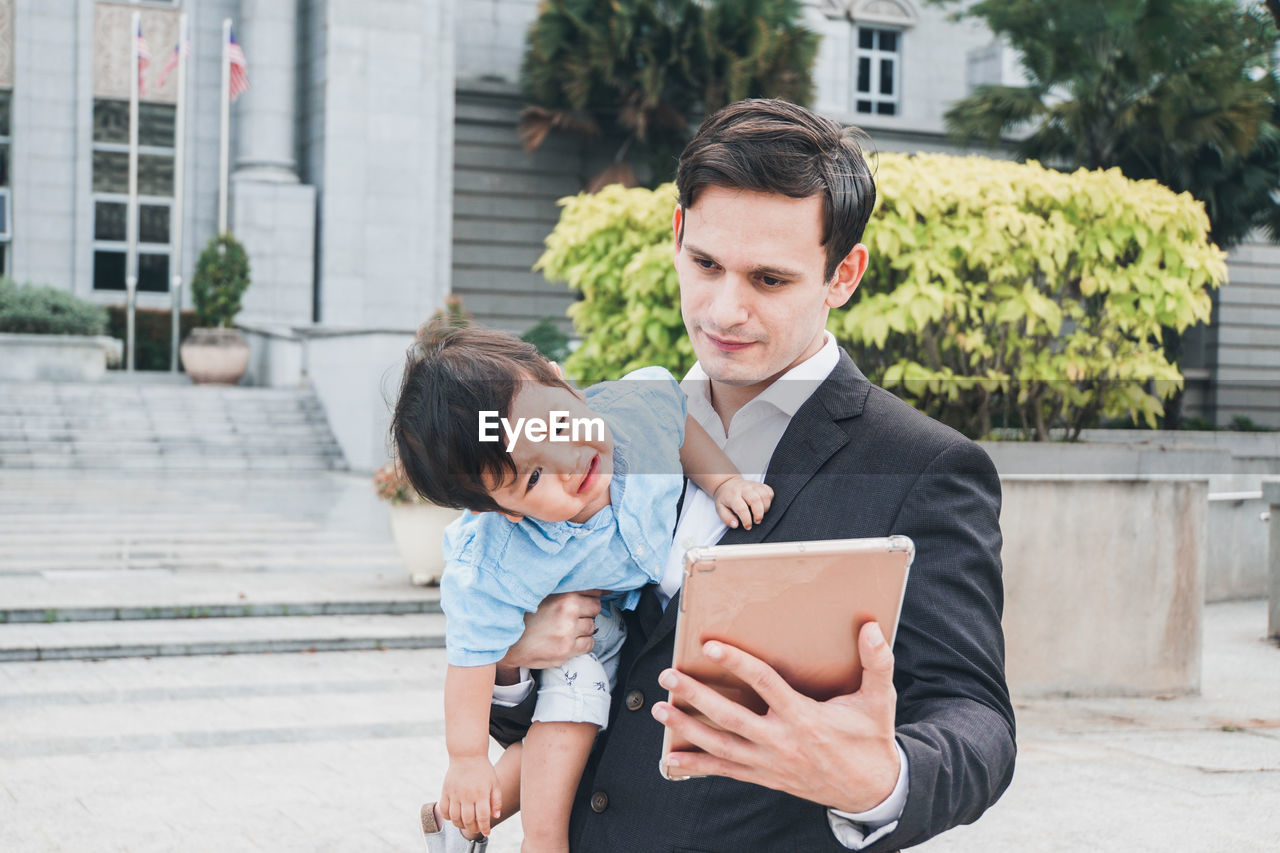 Father carrying son while holding digital tablet