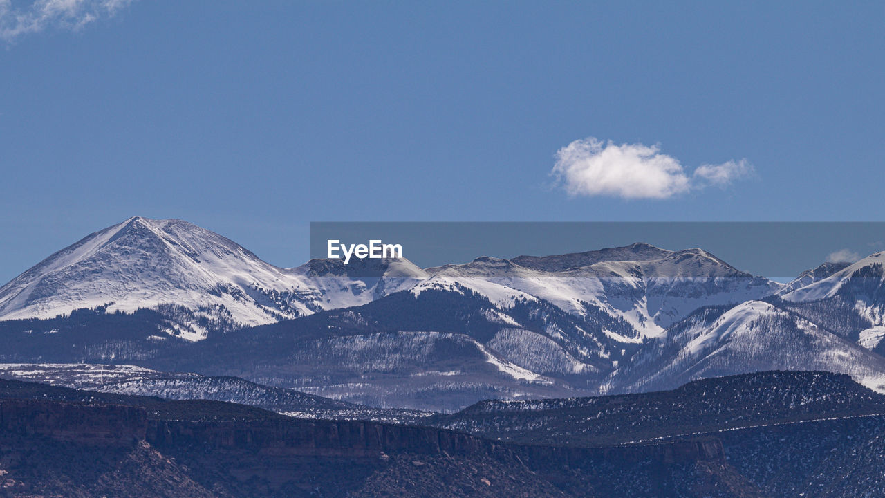 Panoramic scenic view of snow capped mountains with blue sky and a puffy white cloud