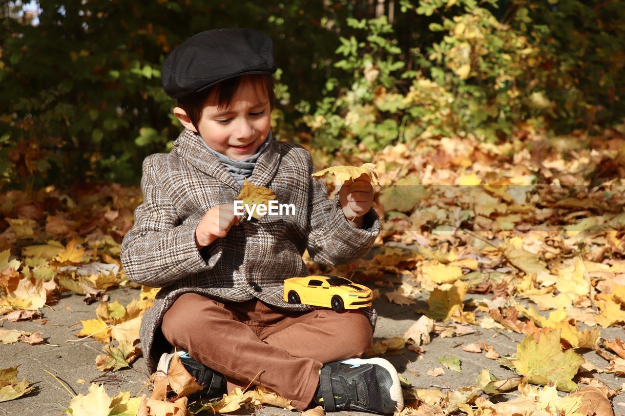 Cute boy holding leaf while sitting outdoors