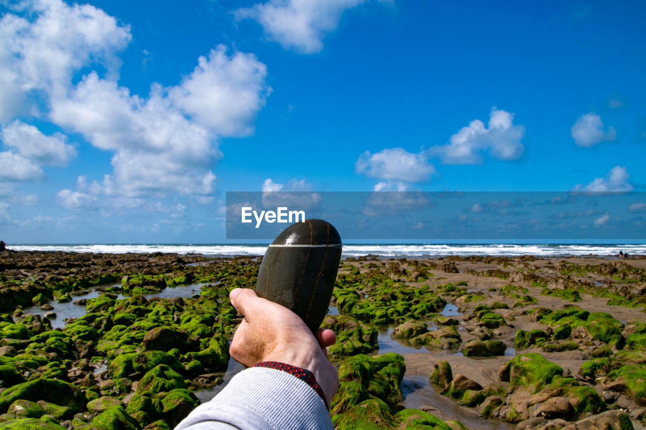 Cropped hand of man holding stone against sky