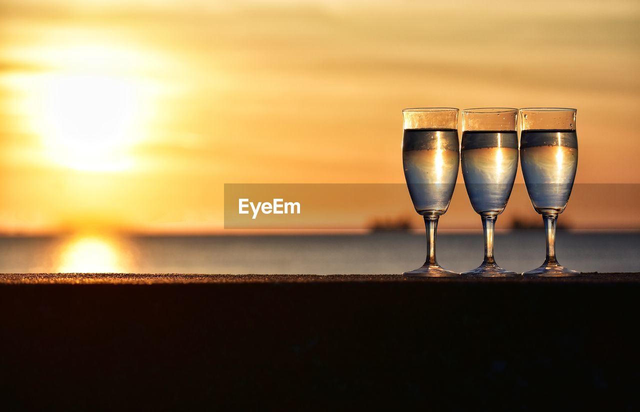 CLOSE-UP OF WINE IN GLASS ON TABLE AGAINST SUNSET