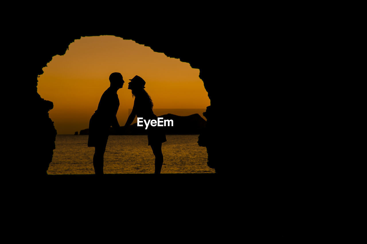 Silhouette couple standing on beach against sky during sunset