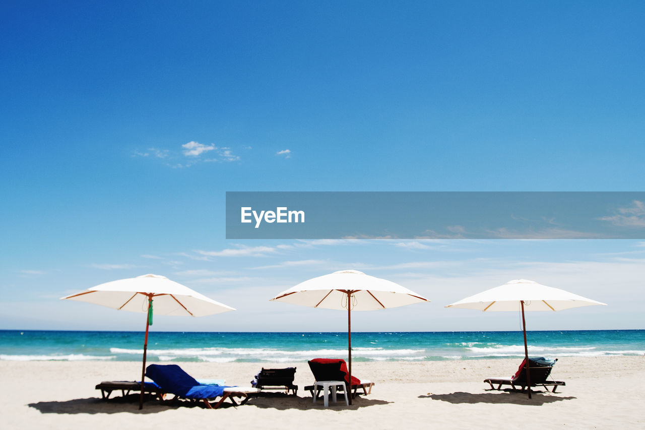 Deck chairs on beach against sky