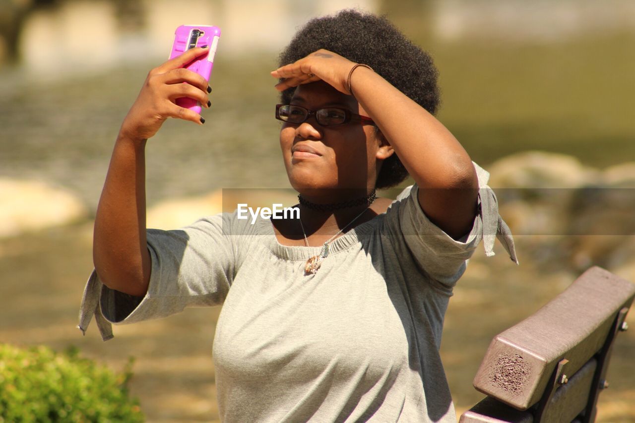 Young woman shielding eyes while taking selfie outdoors