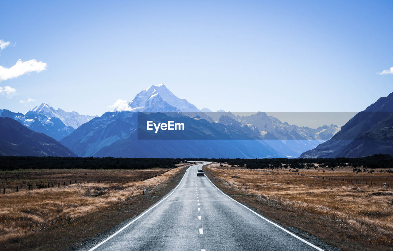 Empty road leading towards mountains against sky