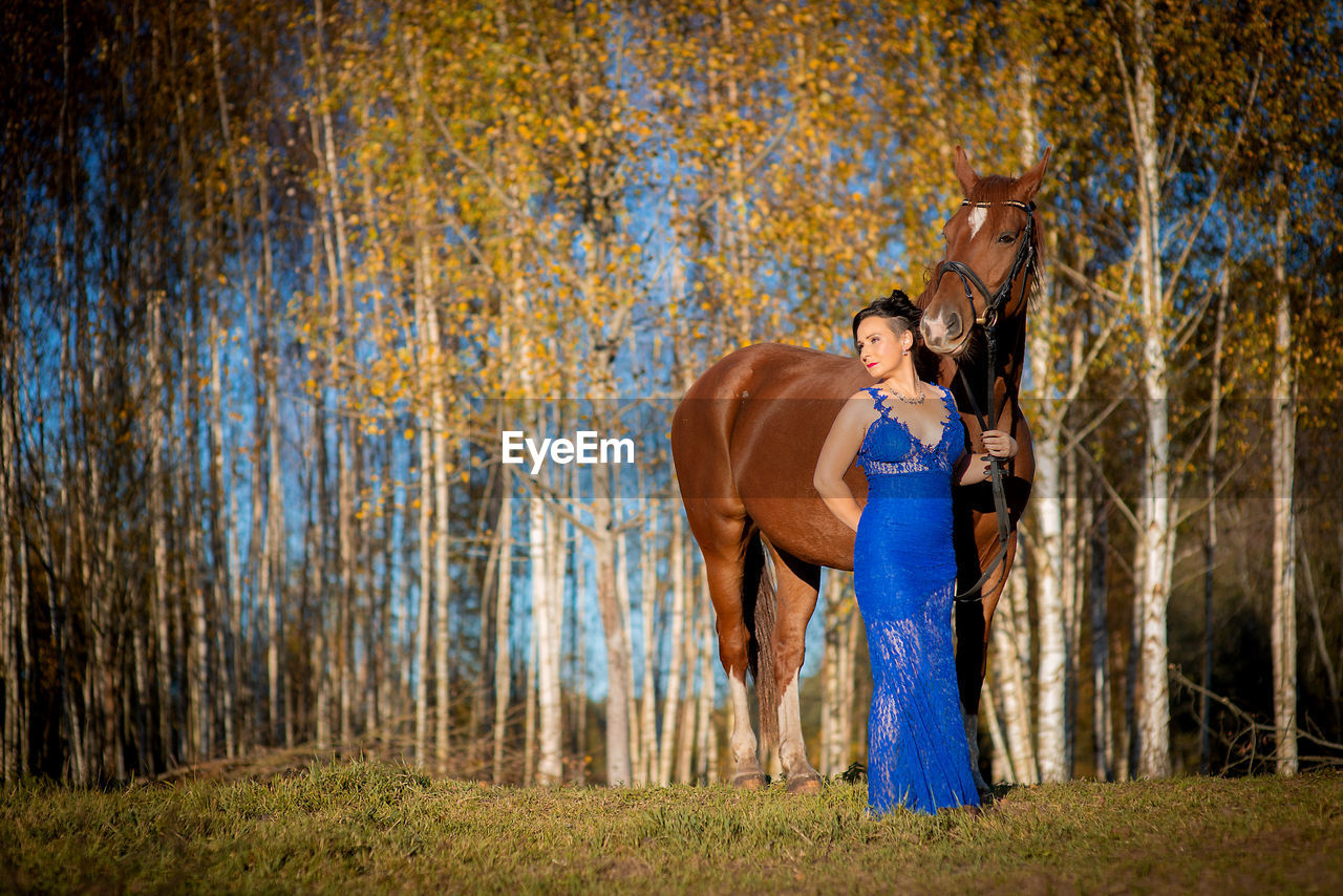 Woman standing by horse at forest during autumn