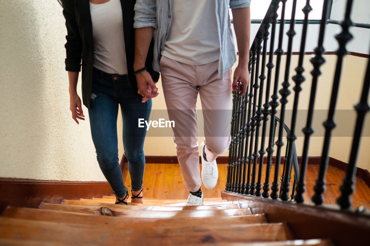 From above anonymous man and woman in casual clothes holding hands and walking up steps at home