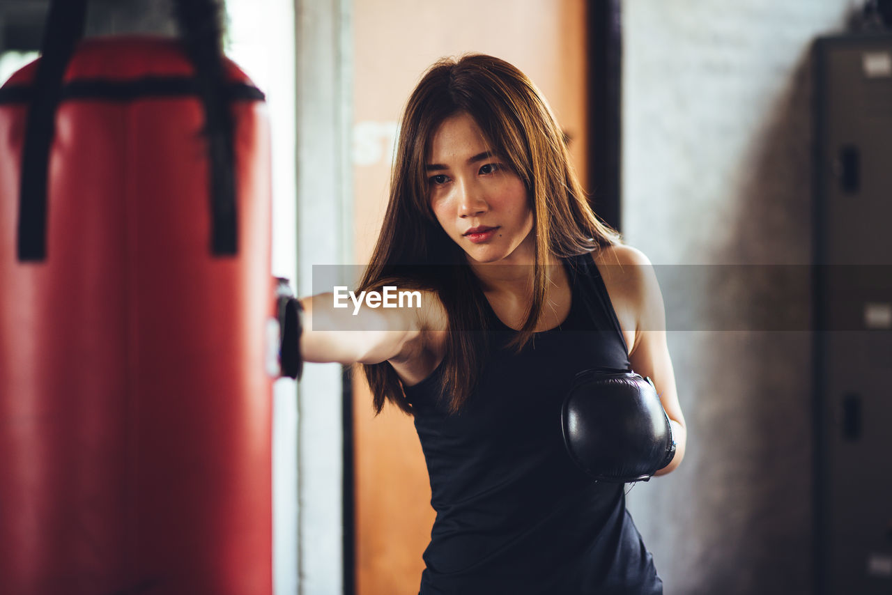 Confident of young woman punching bag while standing in gym