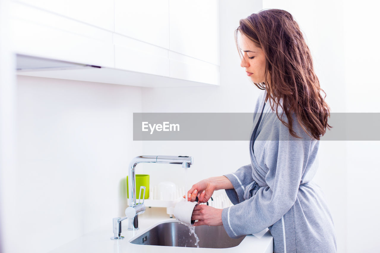 Young woman washing dishes while standing by sink at home