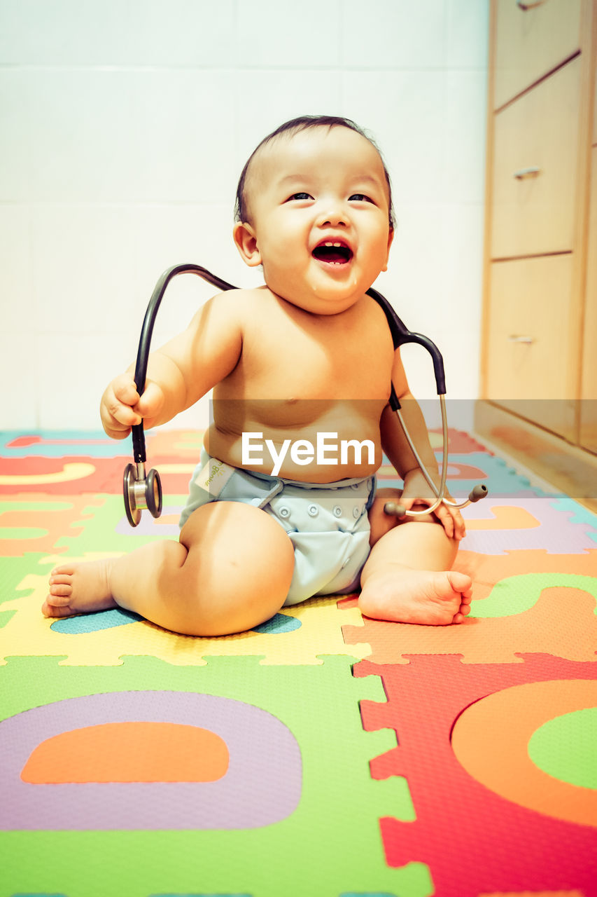Happy baby boy playing with stethoscope on alphabet mat