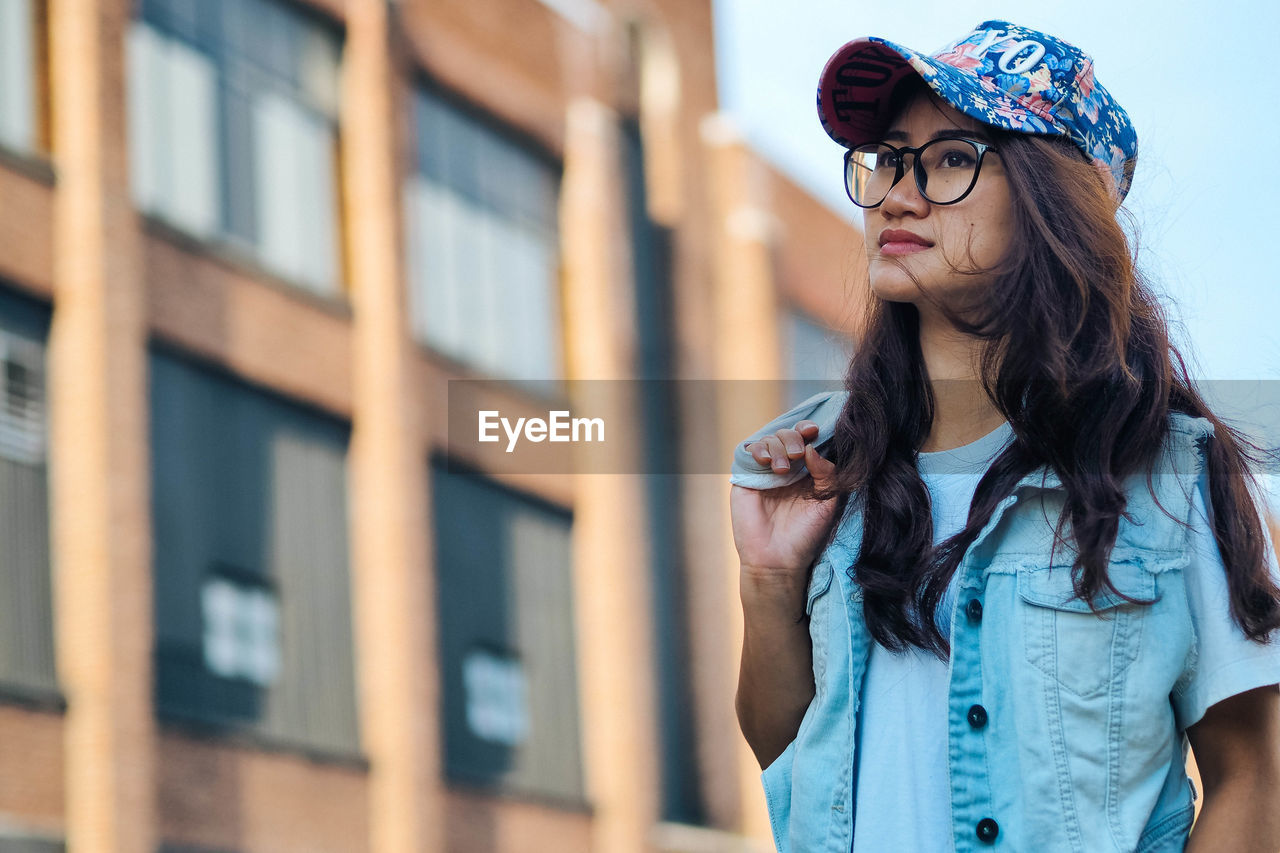 Young woman wearing eyeglasses standing against building