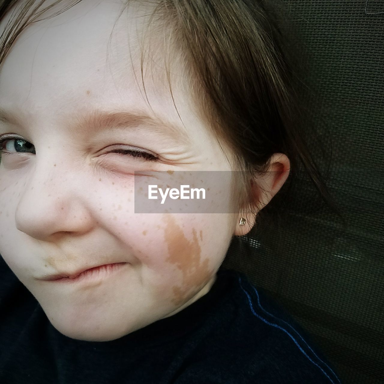 Close-up portrait of girl with freckles on face winking indoor