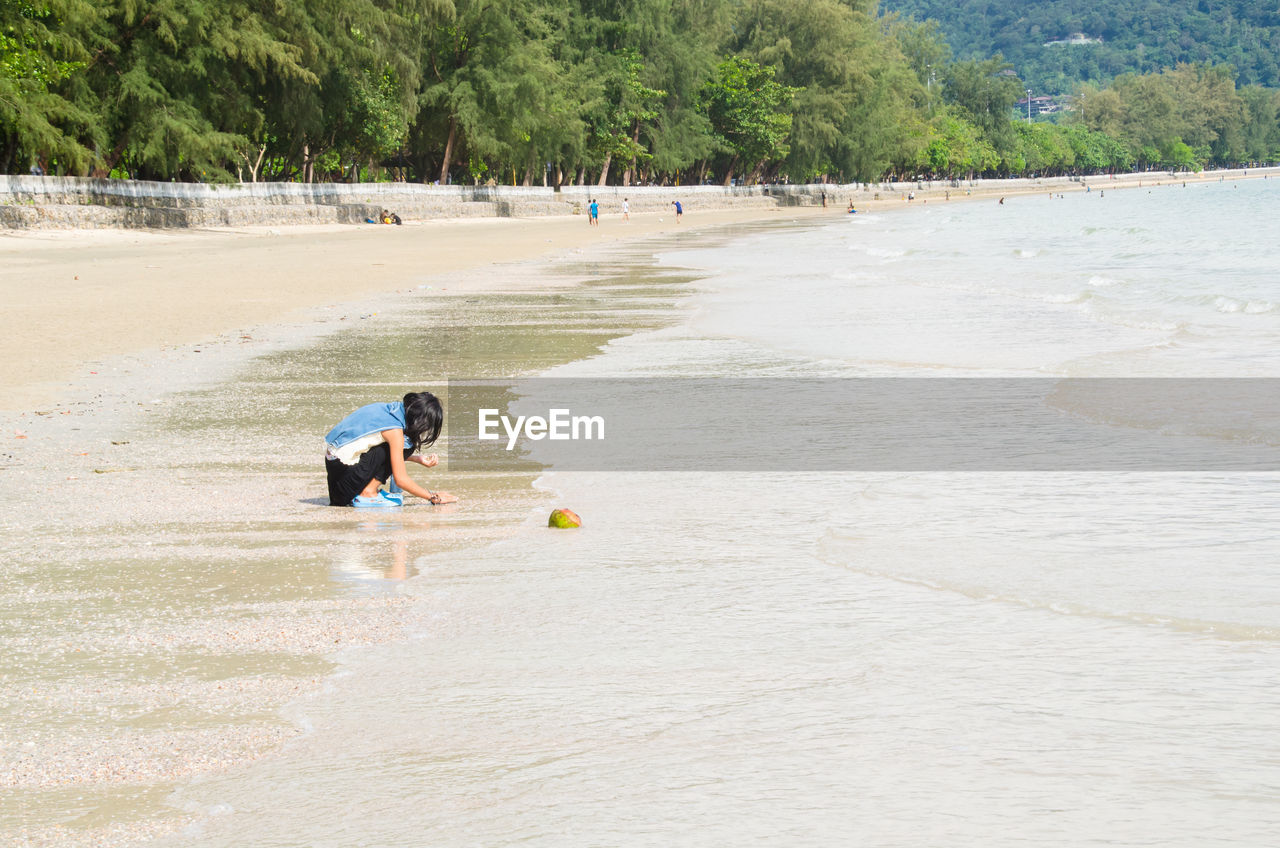 Teenage girl crouching on shore against sea at beach