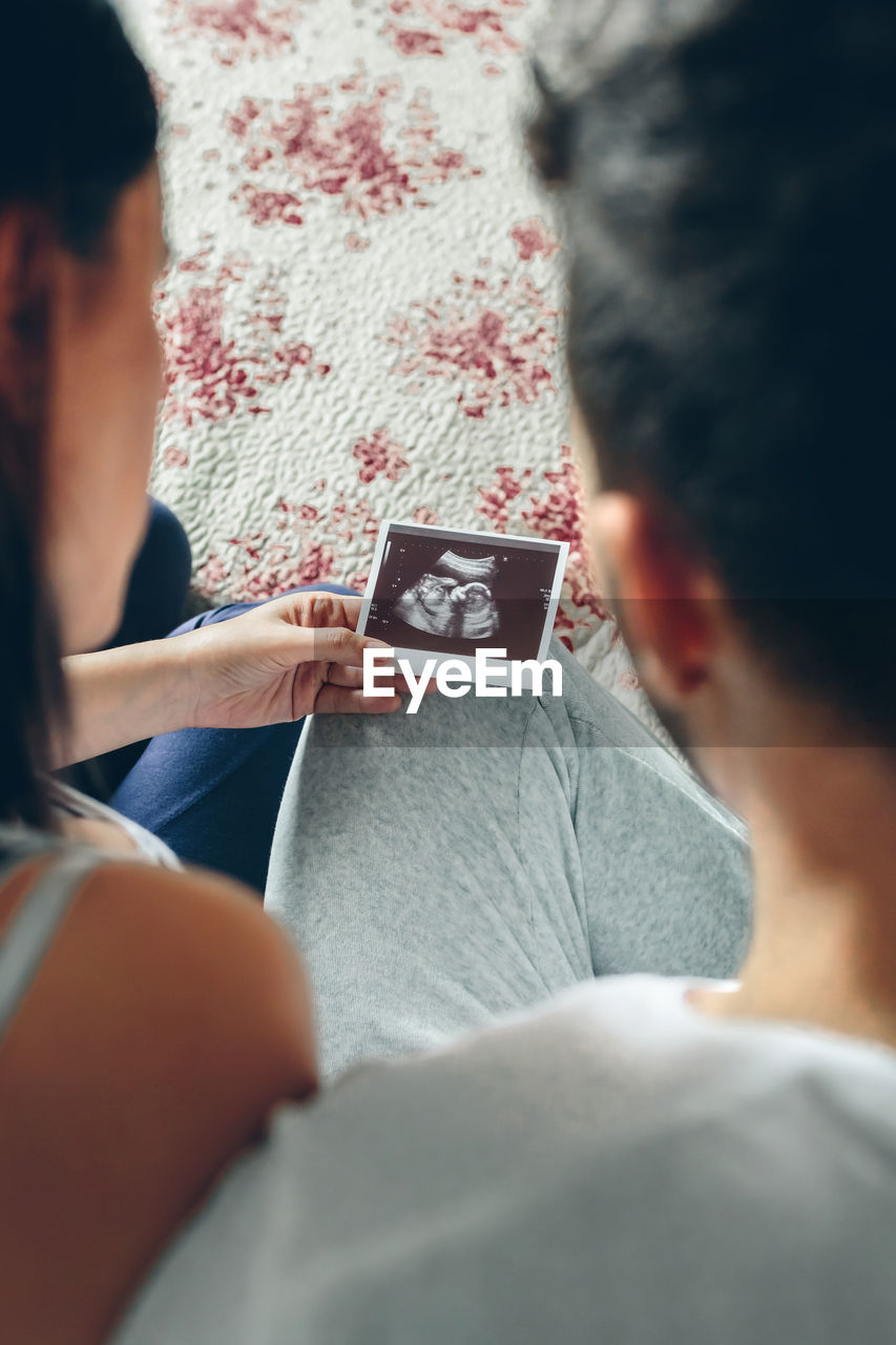 High angle view of couple looking at ultrasound scan on bed