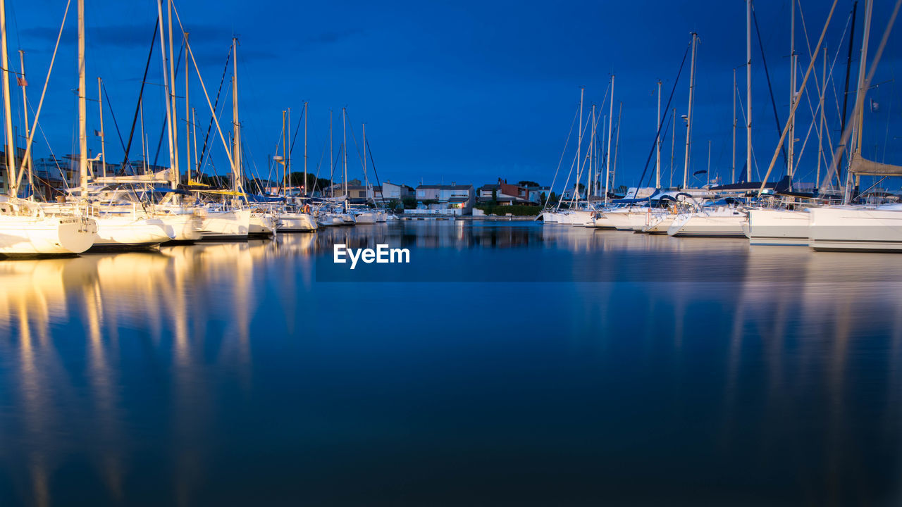 Sailboats moored in harbor against blue sky