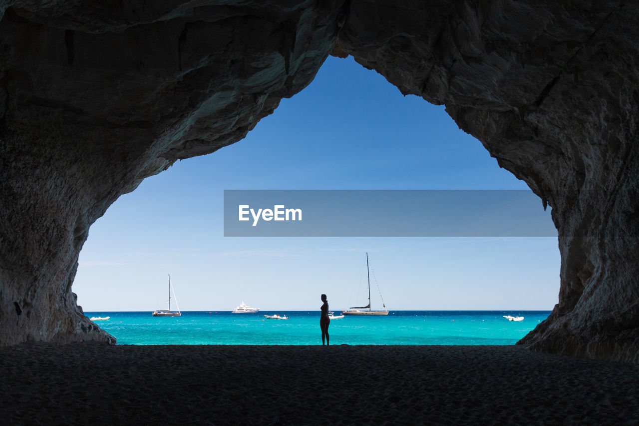 Silhouette woman standing in cave at beach against sea and sky