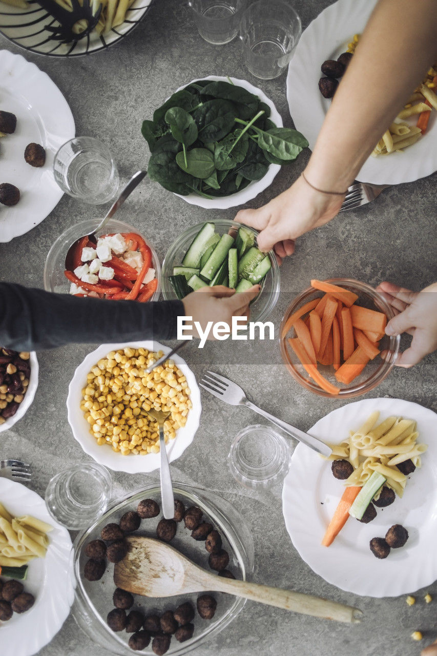 Directly above view of students passing food bowls during lunch time at dining table