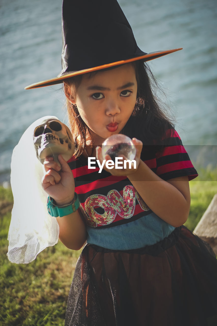 Portrait of girl wearing witch hat holding skull and crystal ball