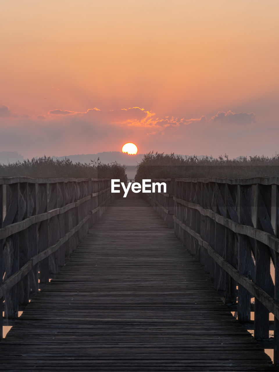 sky, sunset, nature, architecture, wood, landscape, environment, beauty in nature, sun, scenics - nature, tranquility, bridge, cloud, horizon, evening, the way forward, land, water, built structure, sunlight, no people, travel destinations, tranquil scene, pier, boardwalk, outdoors, dawn, footpath, diminishing perspective, travel, dramatic sky, idyllic, railing, orange color, twilight, transportation, tourism, sea, walkway, reflection, non-urban scene, in a row, atmospheric mood, footbridge, rural scene, vanishing point