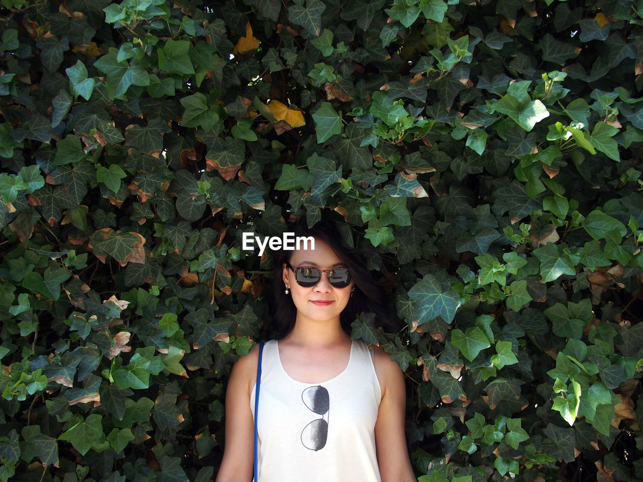 Portrait of young woman wearing sunglasses standing by plants