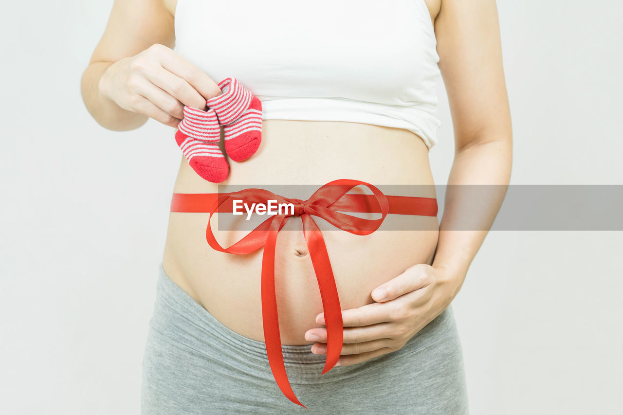 MIDSECTION OF WOMAN HOLDING UMBRELLA AGAINST WHITE BACKGROUND
