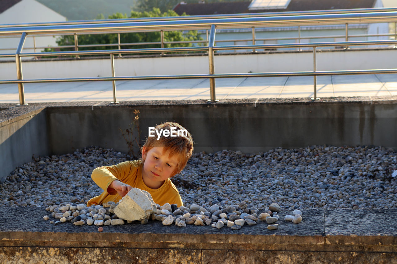 The blond boy is playing with stones. a   boy sits among the stones and carefully arranges them.