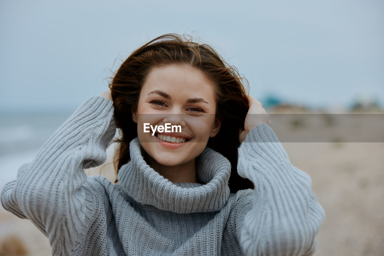 portrait of smiling young woman standing at beach against clear sky