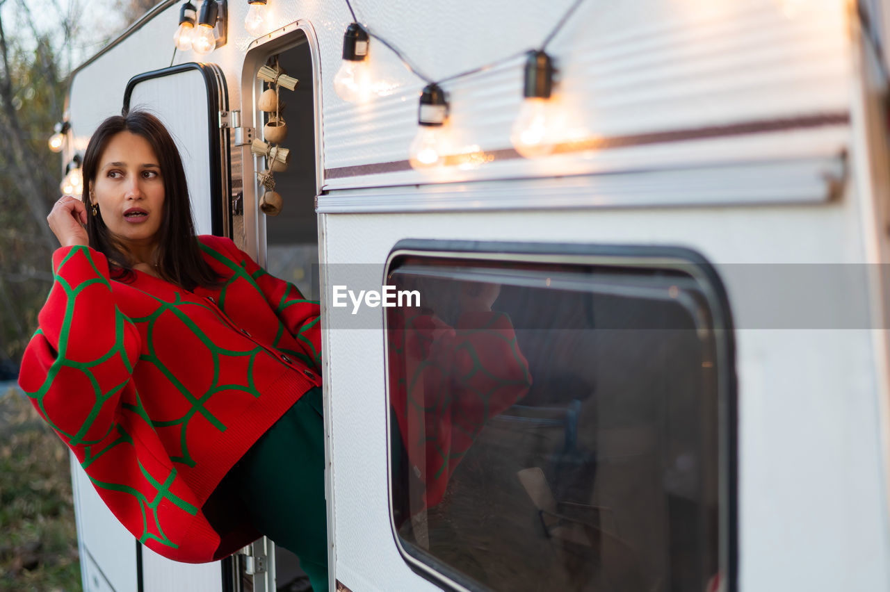 Caucasian woman in oversized red knitted jumper travels in motorhome in autumn