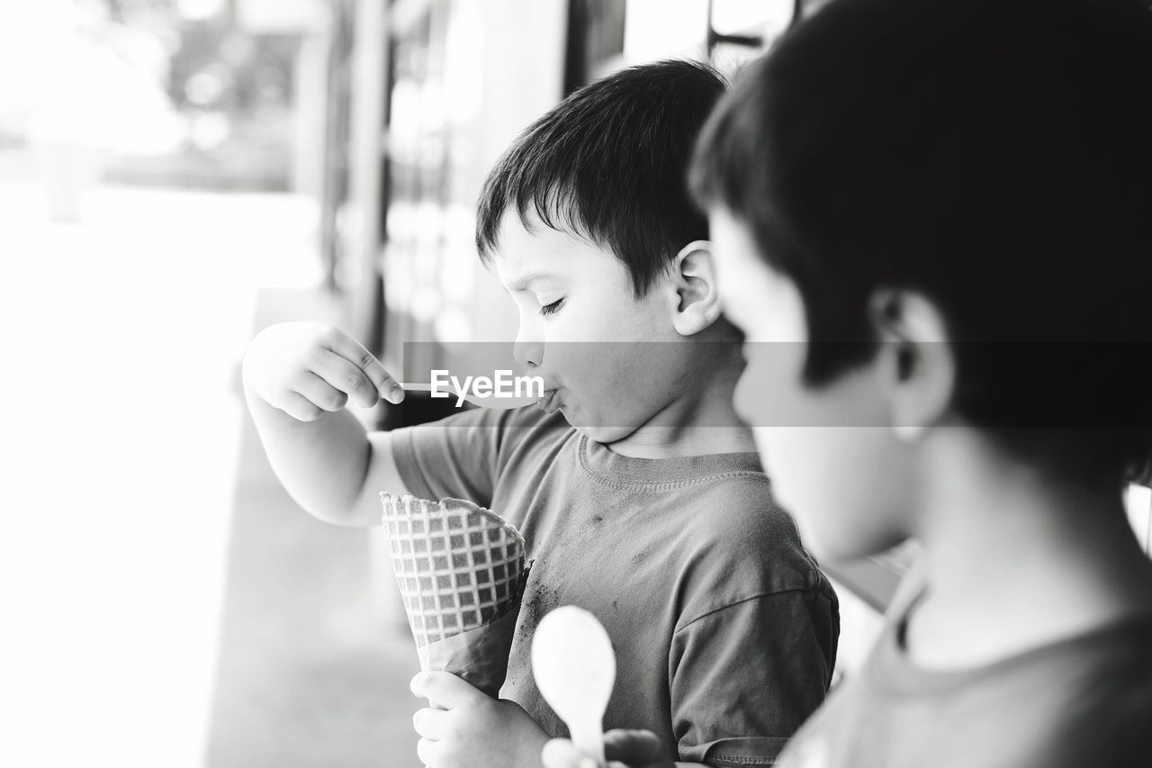 Boy eating ice cream cone with male friend standing outdoors