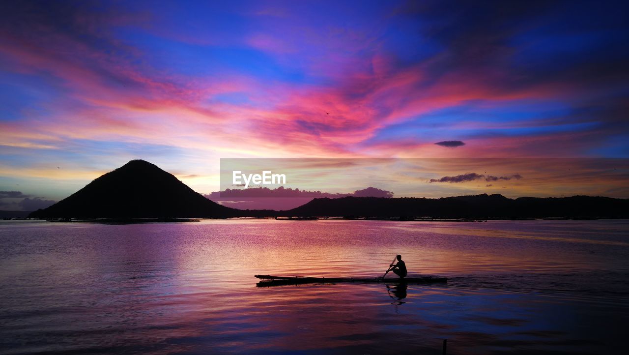 Silhouette man on lake against sky during sunrise 