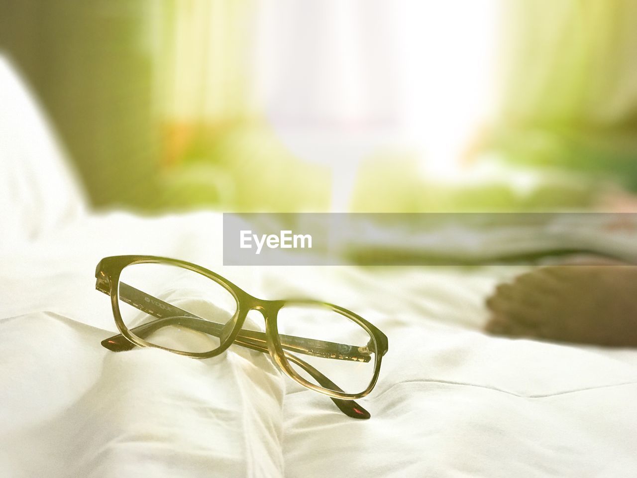 CLOSE-UP OF EYEGLASSES ON BED WITH TABLE